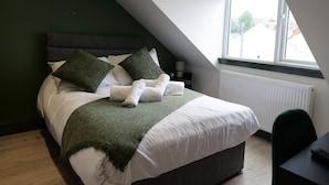 Ein Schlafzimmer mit Bett, Kissen, Decke, Heizkörper, Fenster und Schreibtisch.