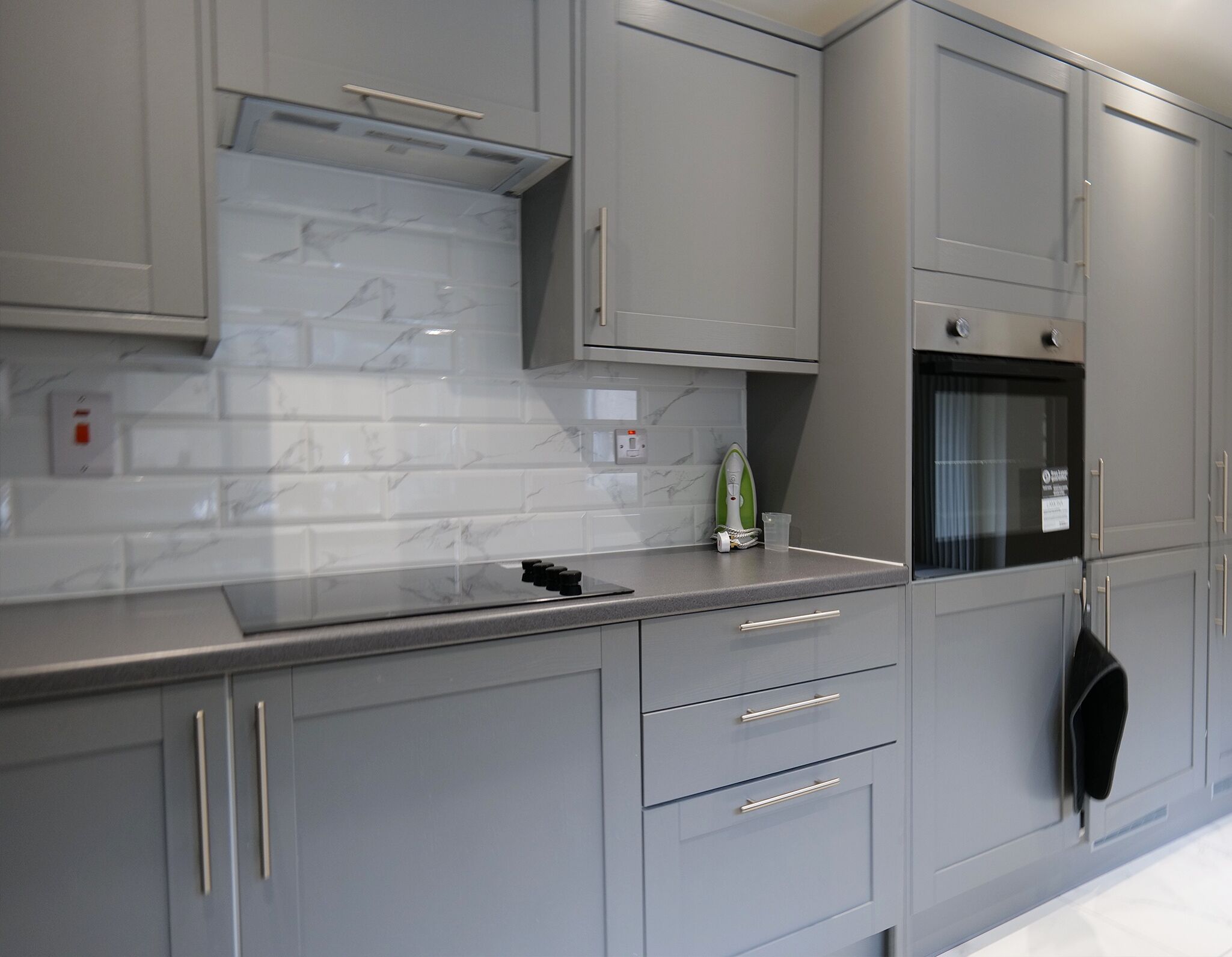 A modern kitchen with grey cabinetry, a marble backsplash, and a built-in oven.