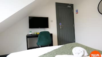 Habitación de hotel con cama, escritorio con televisor, una silla verde y una puerta con letrero.