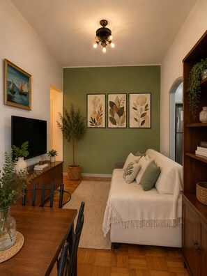 A living room with a sofa, a TV, a dining table with chairs, a plant, and framed artwork on the wall. - Rio Summer - 2 Bedrooms in the Heart of Rio de Janeiro (Rio de Janeiro)