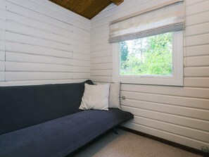 Een kamer met een donkergrijze bank tegen een witte lambrisering, een raam met uitzicht op groen en een houten plafond.