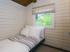 Een kleine kamer met een enkel bed, witte muren en een raam met uitzicht op groen.