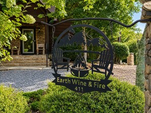 Ein Metallschild mit einem Lagerfeuer und Stühlen, beschriftet mit 'Earth Wine & Fire 411'.