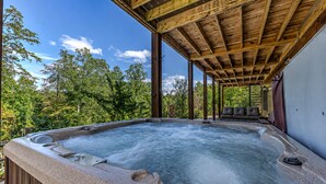 Un jacuzzi con terraza de madera y zona de estar cubierta, rodeado de árboles.