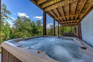 Ein Whirlpool mit Holzterrasse und überdachter Sitzgruppe, umgeben von Bäumen.
