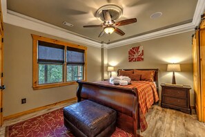 Ein Hotelzimmer mit einem Bett, einem Schreibtisch, einem Stuhl, einem Nachttisch, einer Lampe, einem Deckenventilator, einem Fenster mit Jalousien und einer Tür.