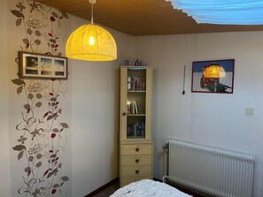 A bedroom with a bed, a radiator, a bookshelf, and a hanging light fixture. - Vacation Rental 1: Cozy & Comfortable on the Ground Floor (Borkum)