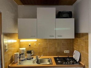 Een kleine keuken met witte kastjes, een gasfornuis, een spoelbak en een magnetron op het aanrecht.