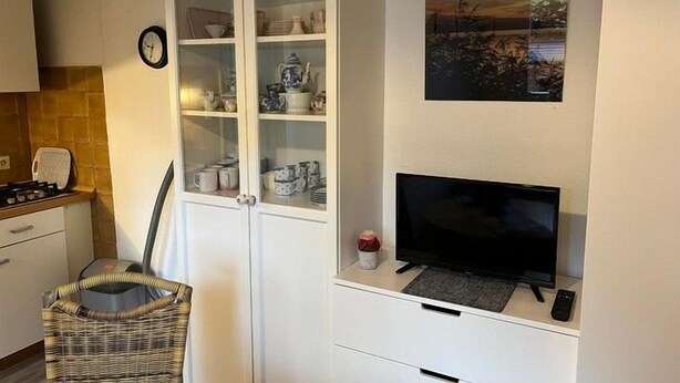 Eine Küche mit einem weißen Schrank, einem Fernseher und einem Korbstuhl.