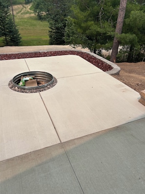 A concrete patio with a circular fire pit surrounded by a stone border. - Enjoyable 2-bedroom cabin with AC in Crivitz near the high Falls flowage (Crivitz)