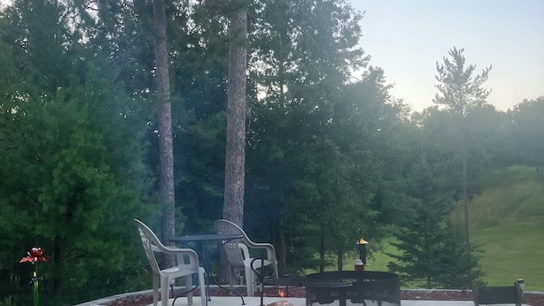 Een terras buiten met vuurkorf, zitgedeelte en omliggende bomen.