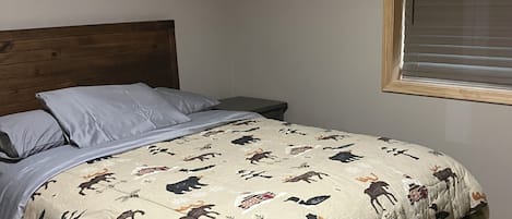 A bed with a patterned bedspread, a wooden headboard, and a nightstand with a lamp.