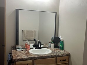 A bathroom with a white sink, a mirror, a towel hanging on the wall, and toiletries on the countertop. - Enjoyable 2-bedroom cabin with AC in Crivitz near the high Falls flowage (Crivitz)