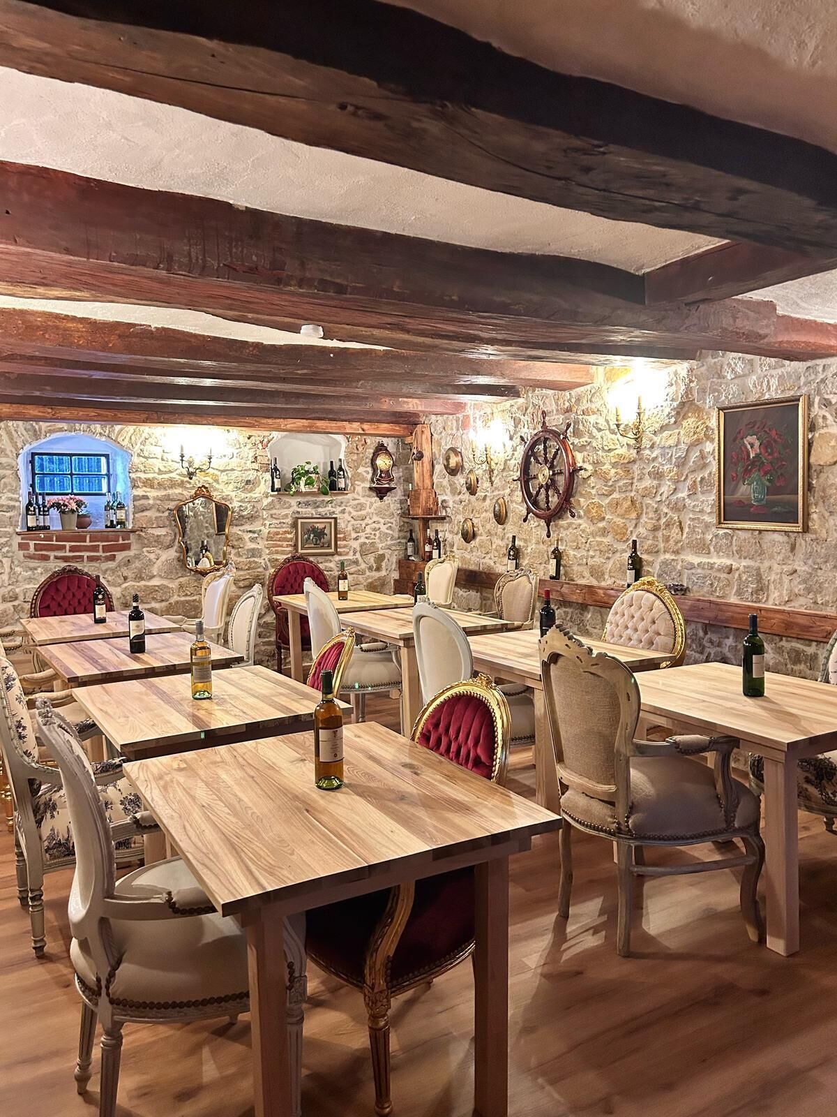 Un restaurant avec des tables et des chaises en bois, des murs en pierre et diverses décorations murales, notamment une horloge et un tableau encadré.
