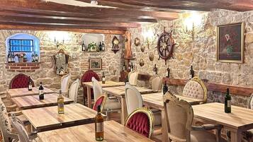 Un restaurant avec des tables et des chaises en bois, des murs en pierre et diverses décorations murales, notamment une horloge et un tableau encadré.