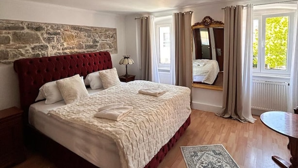 A bedroom with a large bed, stone wall, wooden floor, and a view of greenery outside. - Hotel Goldener Taler (Lörrach)