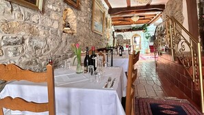 A dining area with stone walls, wooden beams, and a chandelier. Tables are set with white tablecloths and chairs. - Hotel Goldener Taler (Lörrach)
