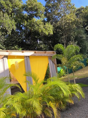 Une structure jaune surmontée d’un toit en bois, entourée de verdure et d’arbres.