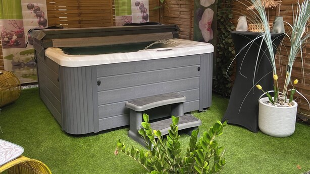 A hot tub with a wooden deck, surrounded by artificial grass, potted plants, and a bamboo basket. - Mon petit coin de paradis - Spa privatif & calme tropical (Morne-à-l'Eau)