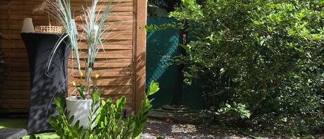 Área de jardim com pérgola de madeira, plantas em vasos e caminho de cascalho.