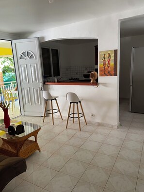 Eine Küche mit einer weißen Tür, zwei weißen Barhocker, einem Glastisch und einem Bild an der Wand.
