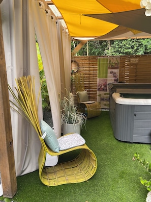 Eine Terrassenfläche mit einem Korbstuhl, einem Whirlpool und einem Holzzaun.
