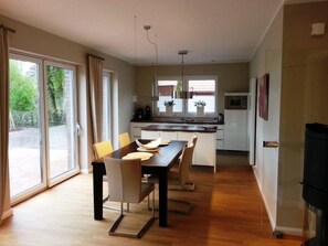 A modern kitchen with a dining area, large windows, and a sliding glass door leading to an outdoor area. - Discover the Scheukelanders Oasis! (Borkum)