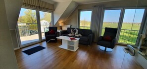 A spacious living room with a modern design, featuring a sofa set, a coffee table, and a view of a green landscape through large windows. - Discover the Scheukelanders Oasis! (Borkum)