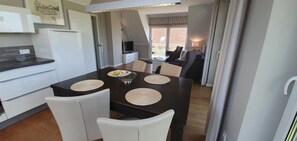 Een moderne keuken met een eethoek, witte stoelen, een donker houten tafel en een televisie op de achtergrond.