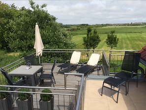 Een terras met buitenmeubilair, waaronder een tafel en stoelen, met uitzicht op een grasveld.