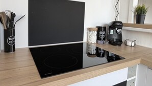 A kitchen with a black induction cooktop, a coffee maker, and a jar of sugar on the counter. - Nice Apartment in Cherbourg for 4 Guests (Cherbourg-en-Cotentin)