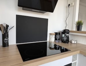 Una cocina con tope de inducción negro, una cafetera y un tarro de azúcar sobre la encimera.