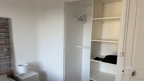 A bedroom with a bed, bedside table, nightstand, and an open closet with shelves. - Nice Apartment in Cherbourg for 4 Guests (Cherbourg-en-Cotentin)