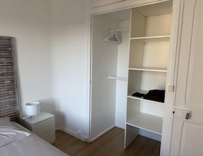 Un dormitorio con cama, mesita de noche y un armario abierto con estantes.