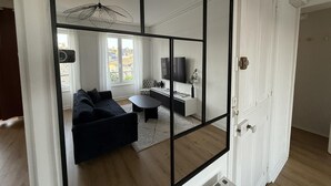 A modern living room with a black-framed mirror, a dark sofa, a round coffee table, and a pendant light. - Nice Apartment in Cherbourg for 4 Guests (Cherbourg-en-Cotentin)