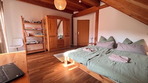 Un dormitorio con una cama de madera, un escritorio con una computadora portátil, una estantería y un armario.