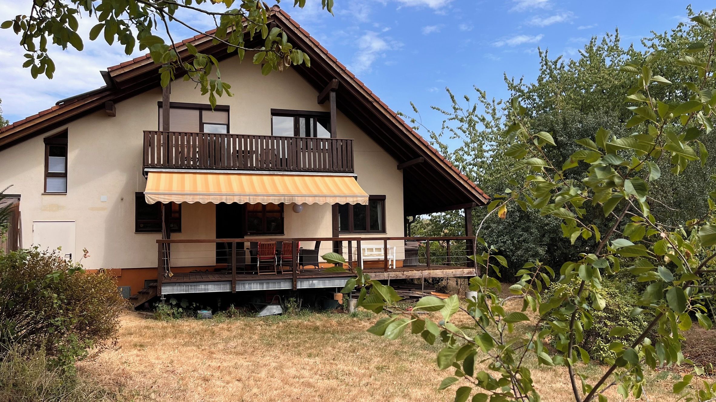 Ein zweistöckiges Haus mit Balkon, überdachter Veranda und kleinem Garten.