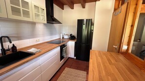 A compact kitchen with white cabinetry, a black refrigerator, and a wooden countertop.