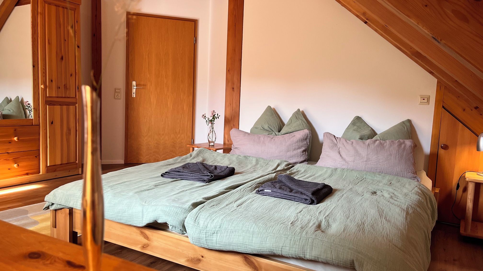 Ein Schlafzimmer mit einem Holzbettgestell, zwei Kissen, einem Nachttisch und einem Beistelltisch.