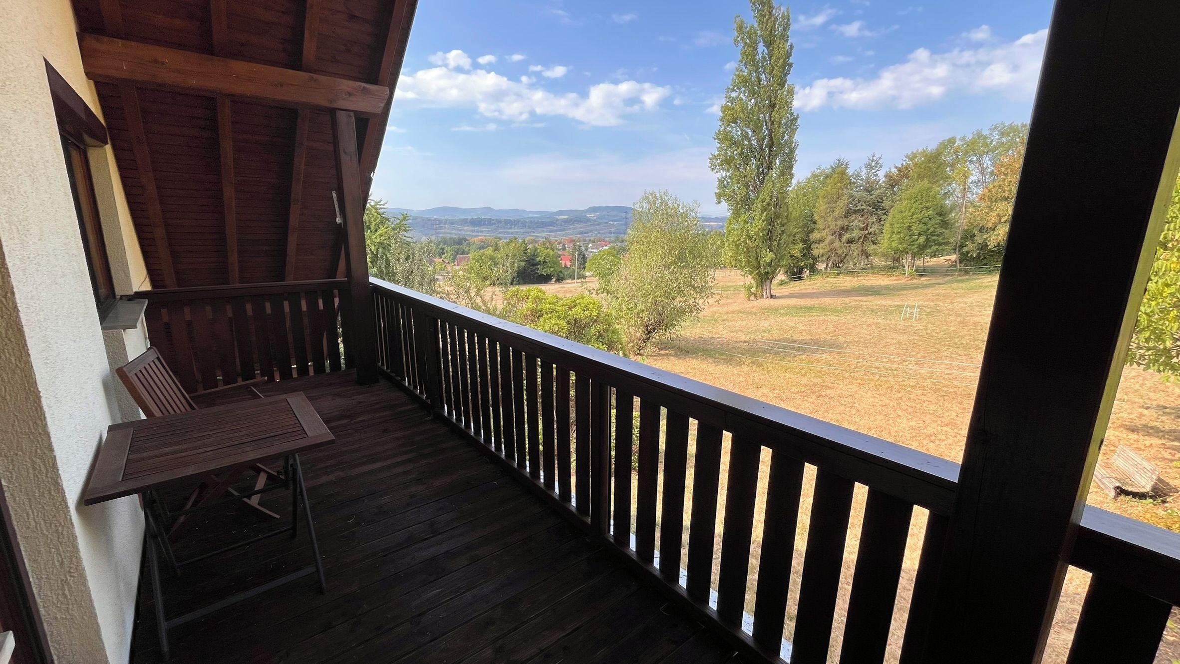 Ein Holzbalkon mit Blick auf eine ländliche Landschaft, einschließlich Bäume und ferner Hügel.