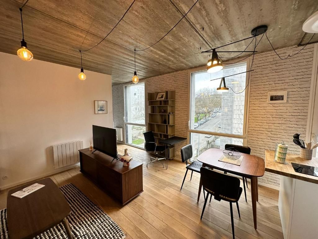 Een moderne woonkamer met een bank, een televisie, een eettafel met stoelen en een keuken met een aanrecht en apparatuur.