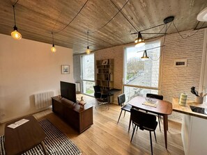 A modern living room with a sofa, a TV, a dining table with chairs, and a kitchen area with a countertop and appliances. - Apartment in the city center—everything is nearby. (Brest)