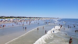 A beach with people swimming and walking along the shore, umbrellas, and beach chairs.