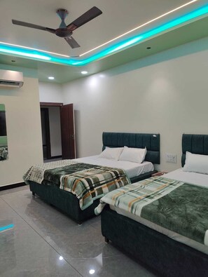 Habitación de hotel con dos camas, ventilador de techo, iluminación empotrada y suelo de baldosas.