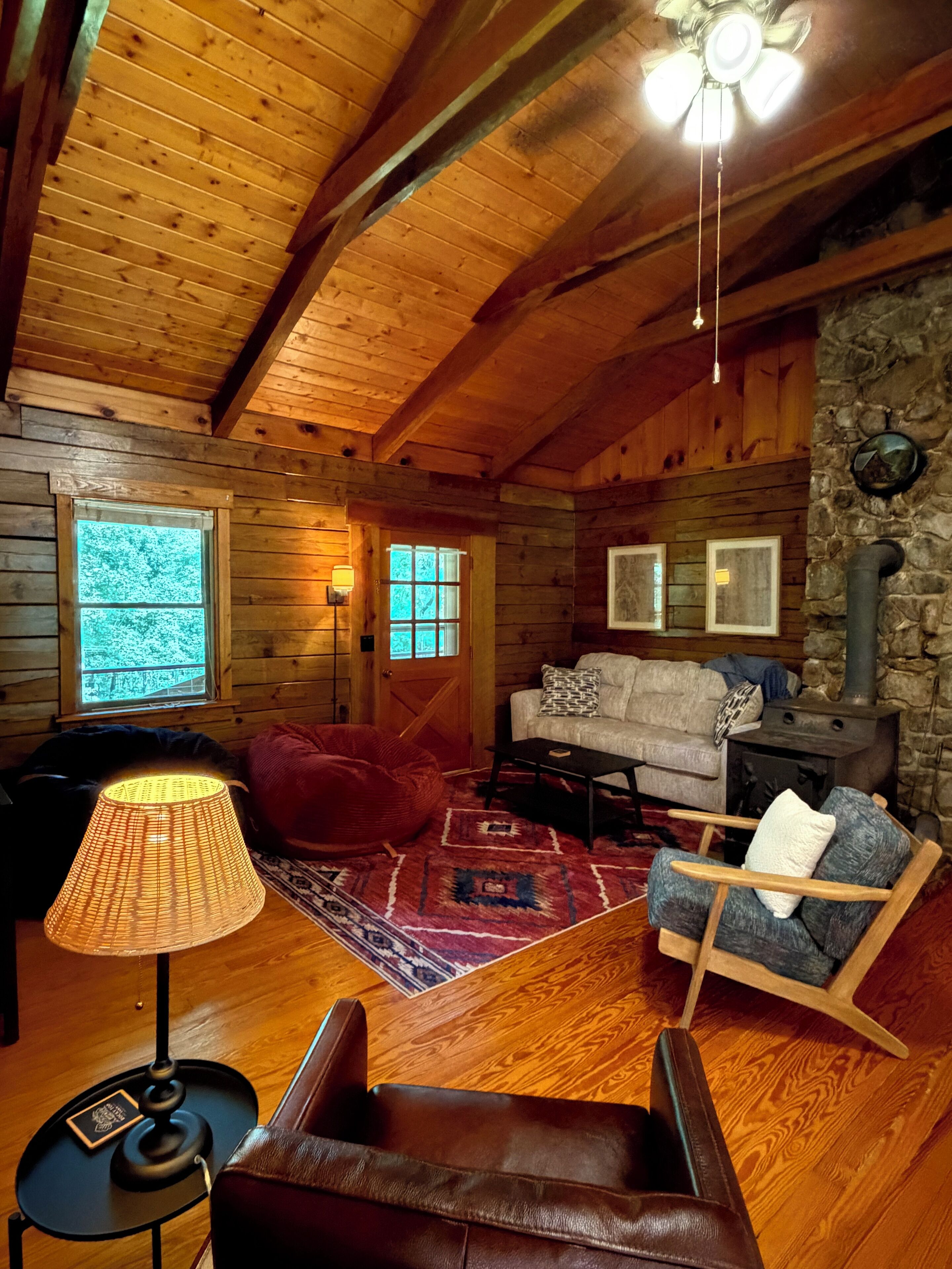 L’intérieur d’un chalet accueillant, avec des murs en bois, une cheminée en pierre, un canapé, un fauteuil en cuir et une lampe.