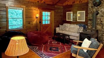 L’intérieur d’un chalet accueillant, avec des murs en bois, une cheminée en pierre, un canapé, un fauteuil en cuir et une lampe.
