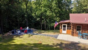 Eine Hütte mit einer Terrasse und Sitzgelegenheiten im Freien, umgeben von einem Wald.