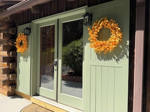 A wooden building with a green door, two black lanterns, and a wreath on each door.