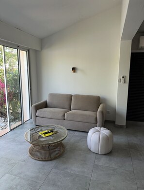 Ein modernes Wohnzimmer mit einer Couch, einem runden Korbtisch und einem weißen Pouf.