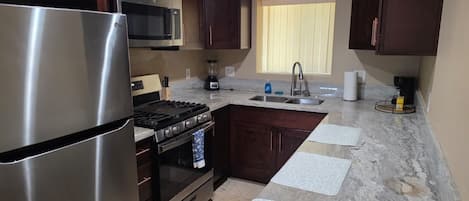 Una cocina con armarios de madera oscura, electrodomésticos de acero inoxidable, encimera de granito y una ventana con persianas.